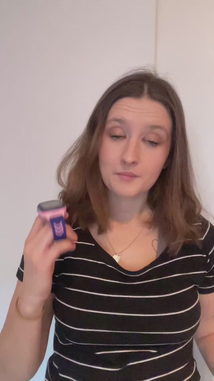 Žena v pruhovaném tričku drží v ruce dětské hodinky KLOKI a vysvětluje, proč si je vybrala pro své dítě. Video má neutrální, světlé pozadí a žena komunikuje přímo směrem ke kameře.